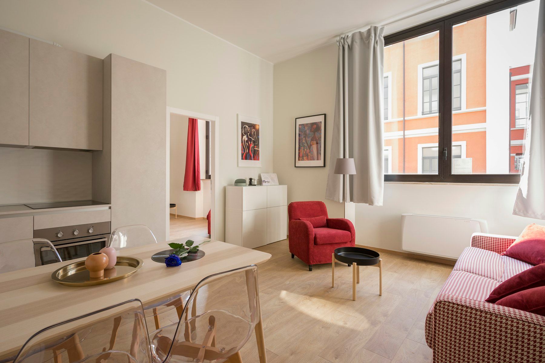 Salón comedor luminoso con cocina abierta, sofá y butaca roja