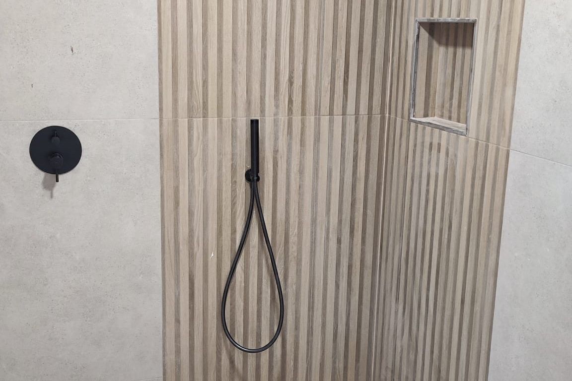 Ducha terminada con revestimiento de listones efecto madera, grifería negra empotrada y hornacina