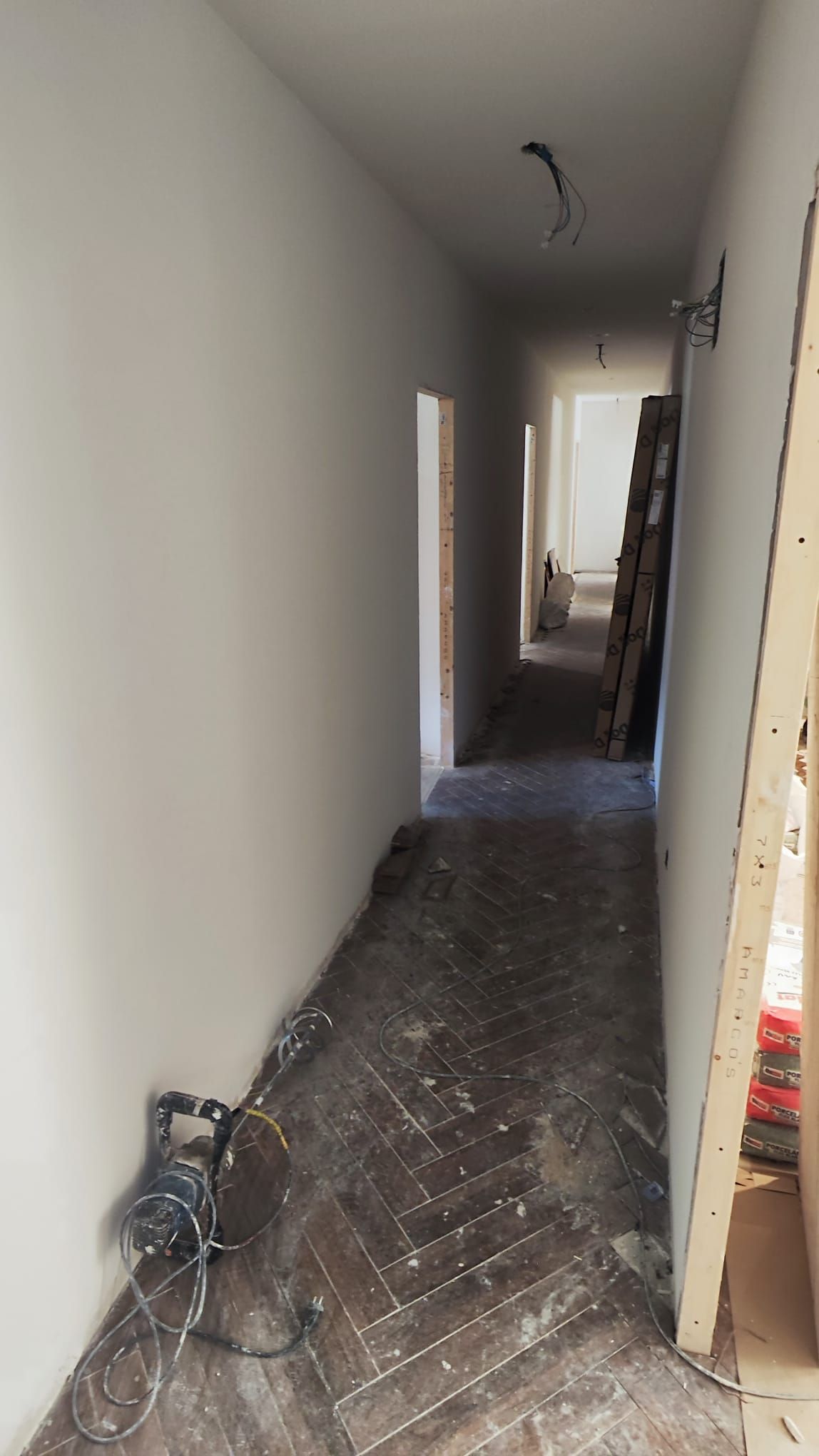 Pasillo de un piso en obra con suelo de parqué en espiga y las herramientas de trabajo