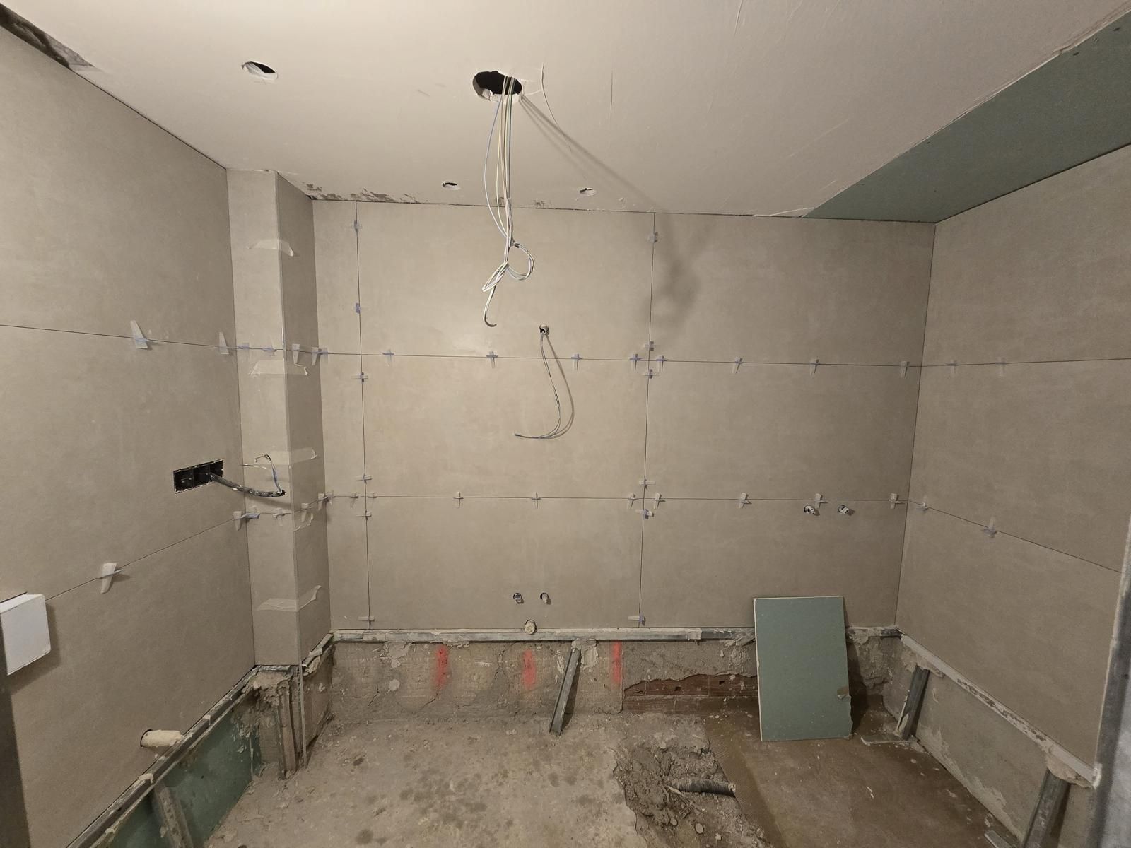 Baño en obra con las paredes alicatadas en porcelánico gris de gran formato y las tomas de agua preparadas
