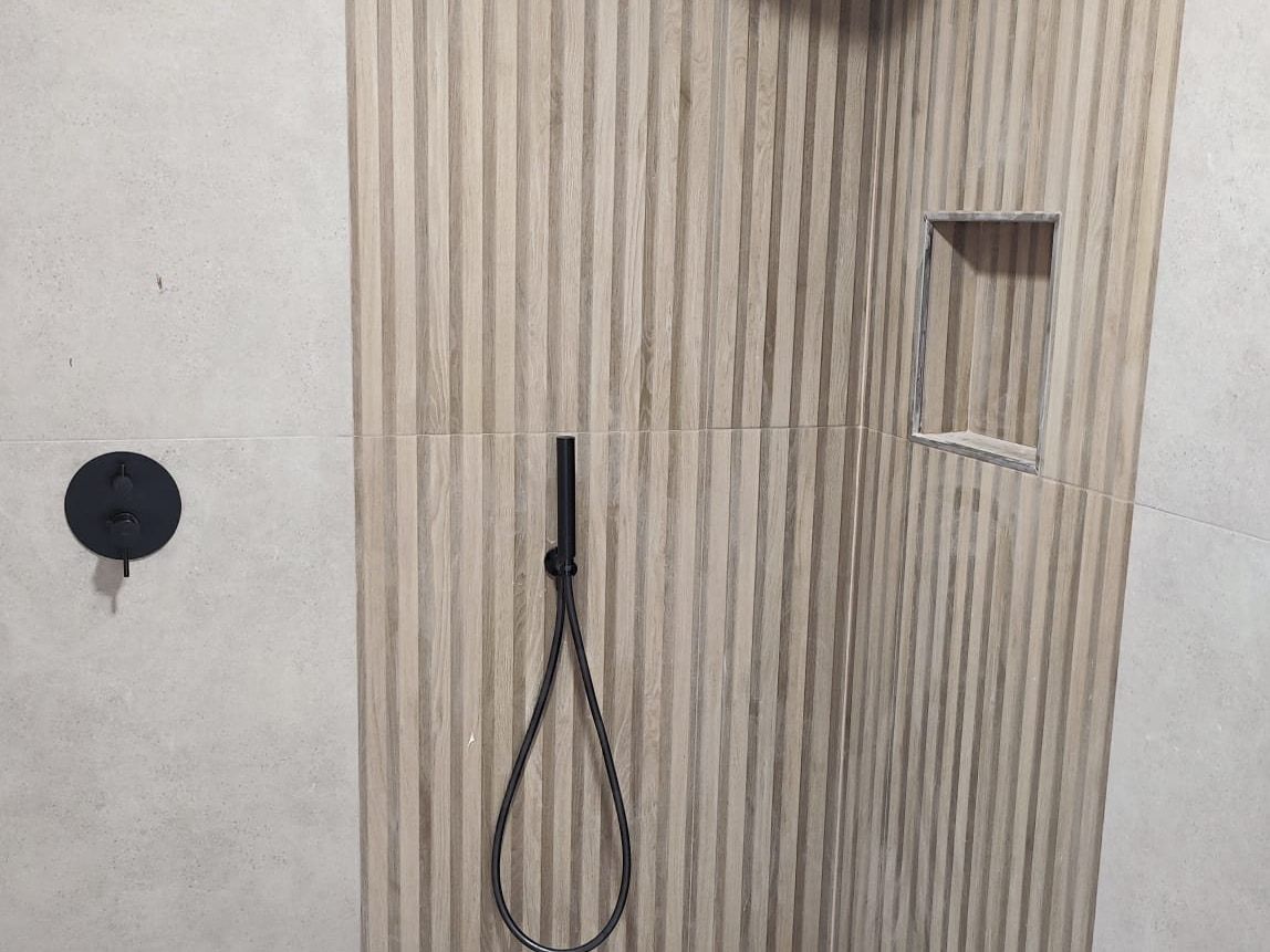 Baño terminado con ducha de listones efecto madera, grifería negra empotrada e inodoro blanco