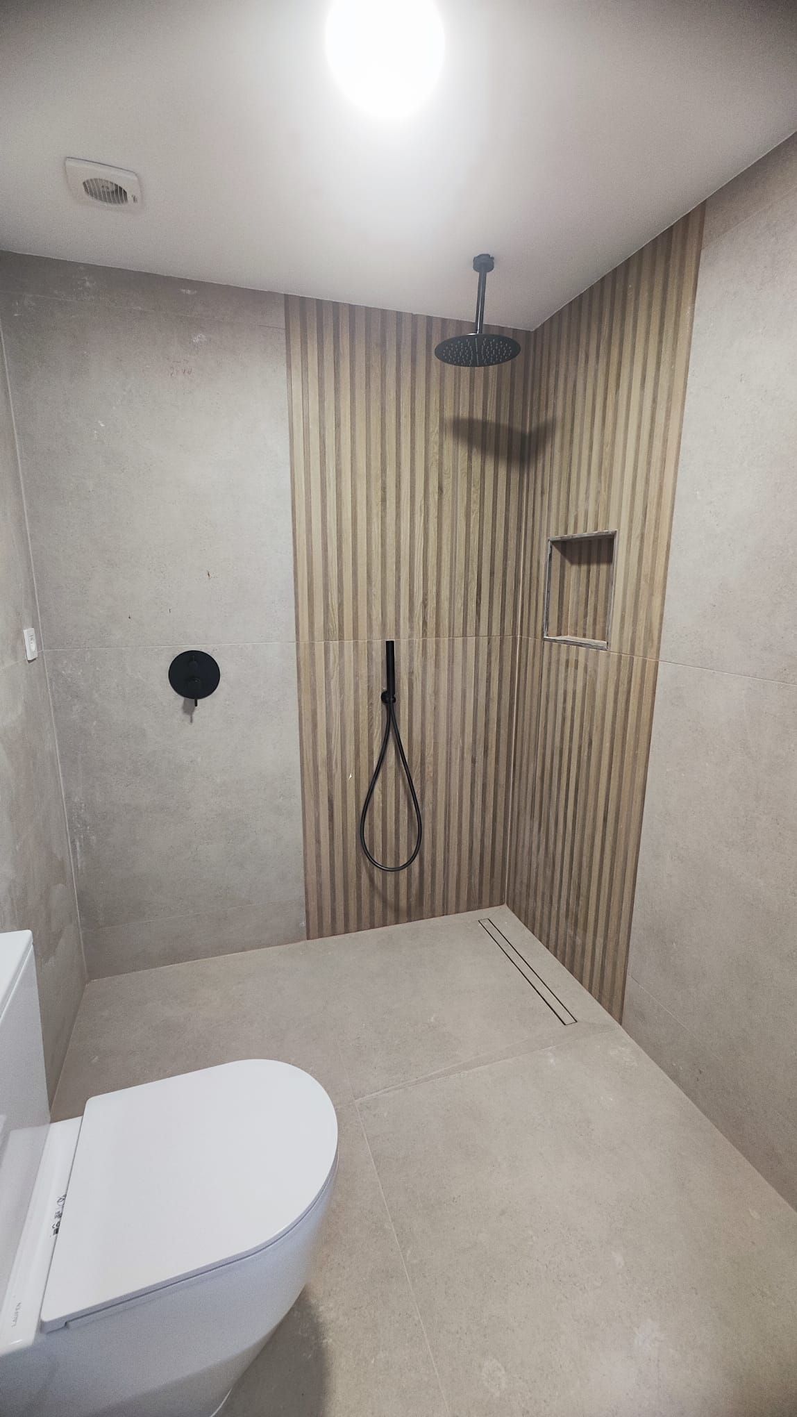 Baño terminado con ducha a ras de suelo y revestimiento de listones efecto madera