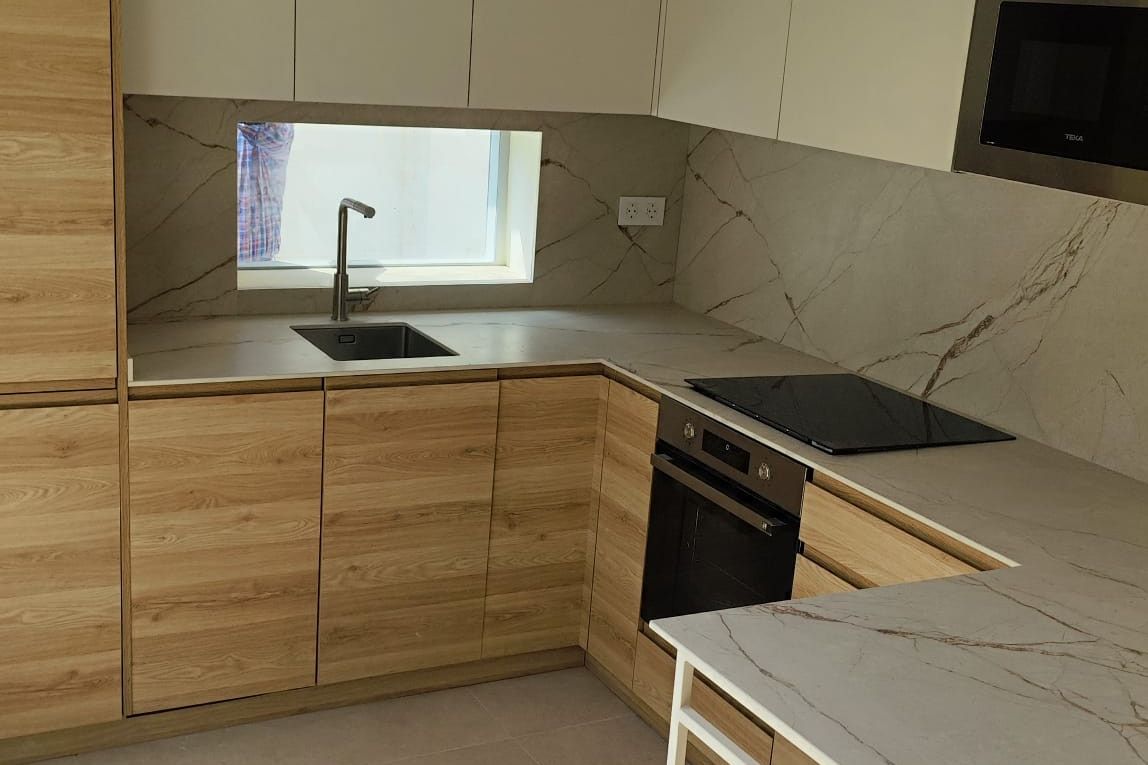 Cocina terminada con muebles de madera clara, altos blancos y mesa auxiliar con encimera de efecto mármol