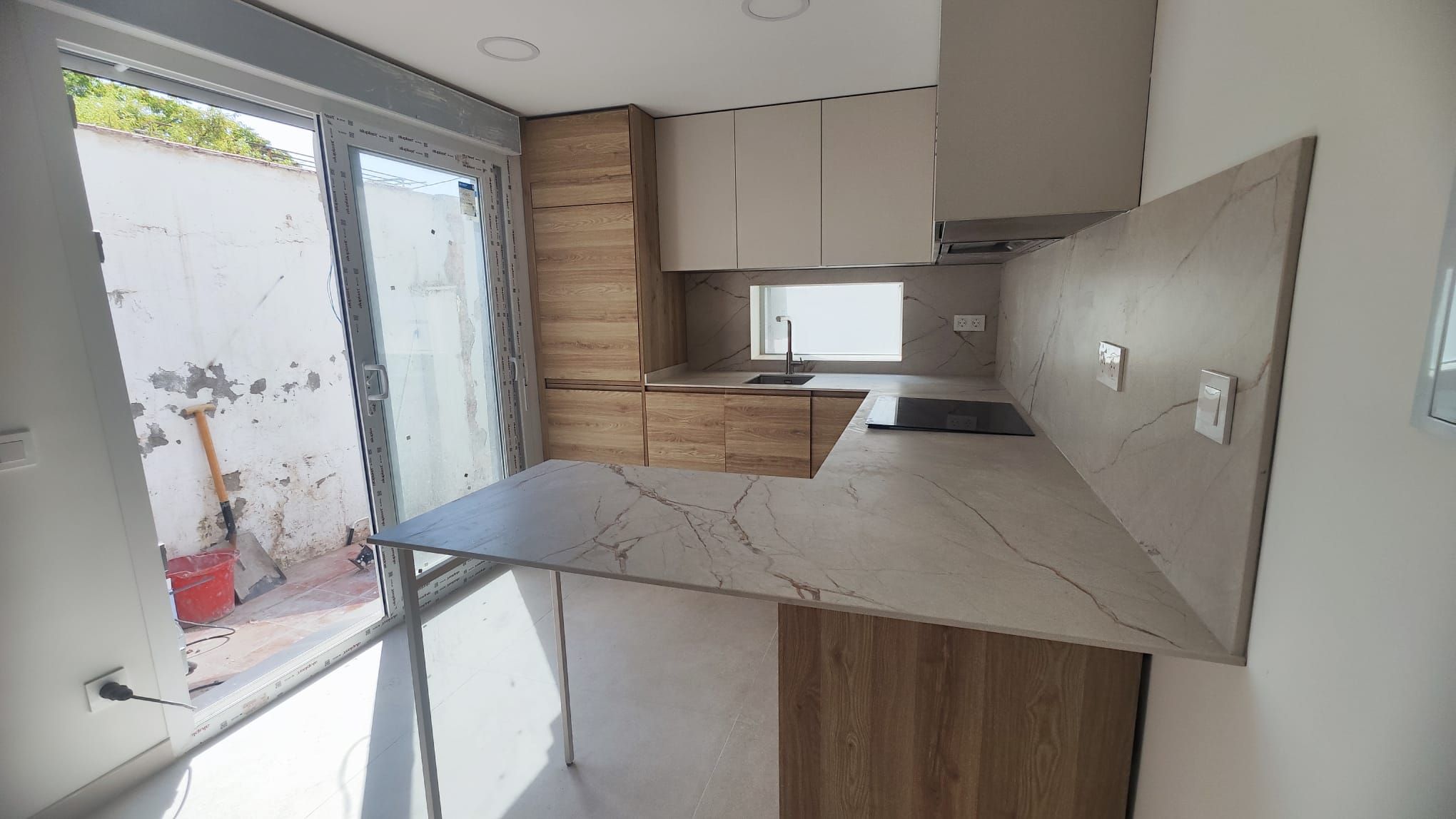Cocina terminada en L con península de efecto mármol junto a la puerta acristalada del patio