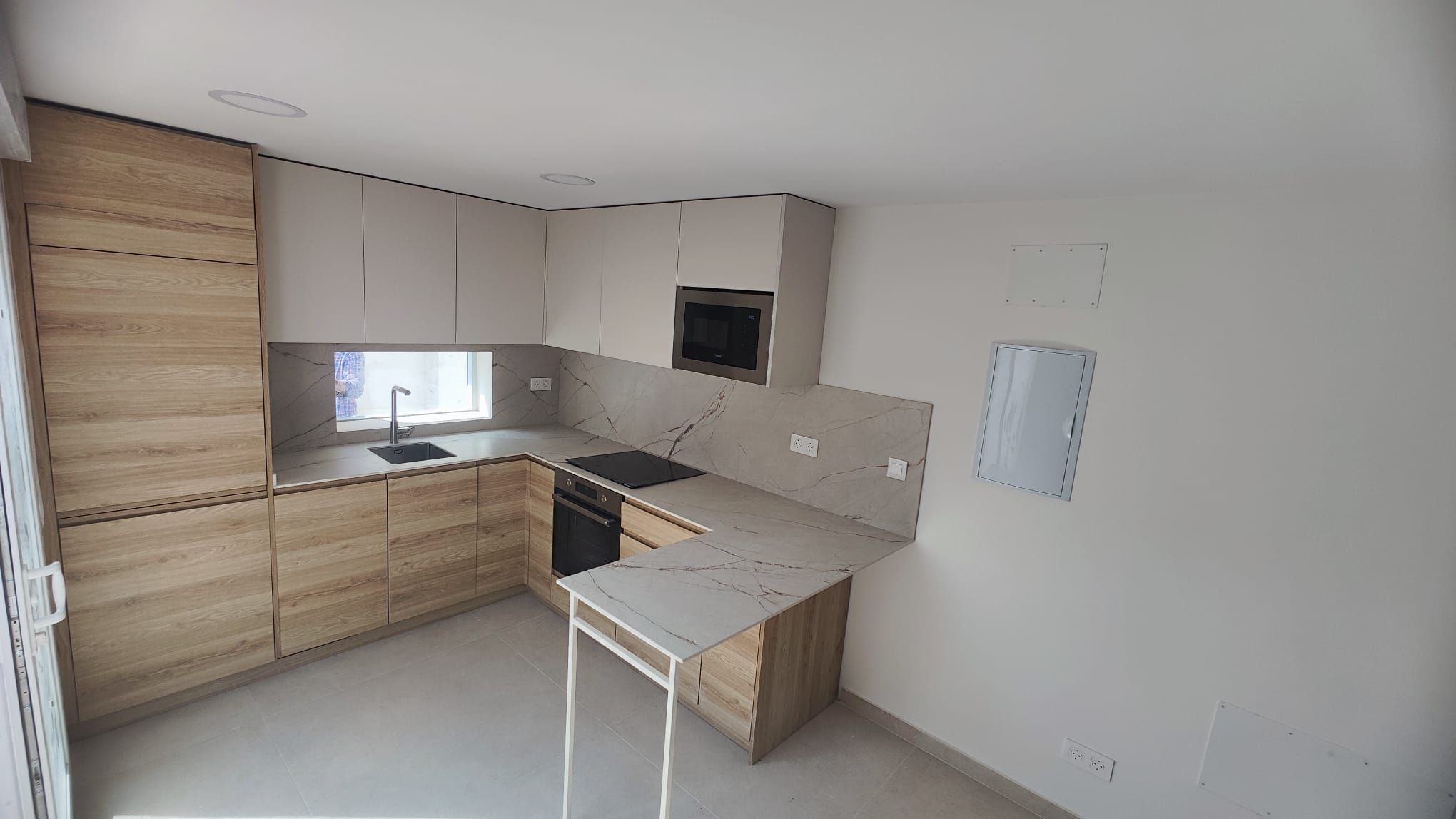Cocina terminada en L con muebles de madera clara, altos blancos y península