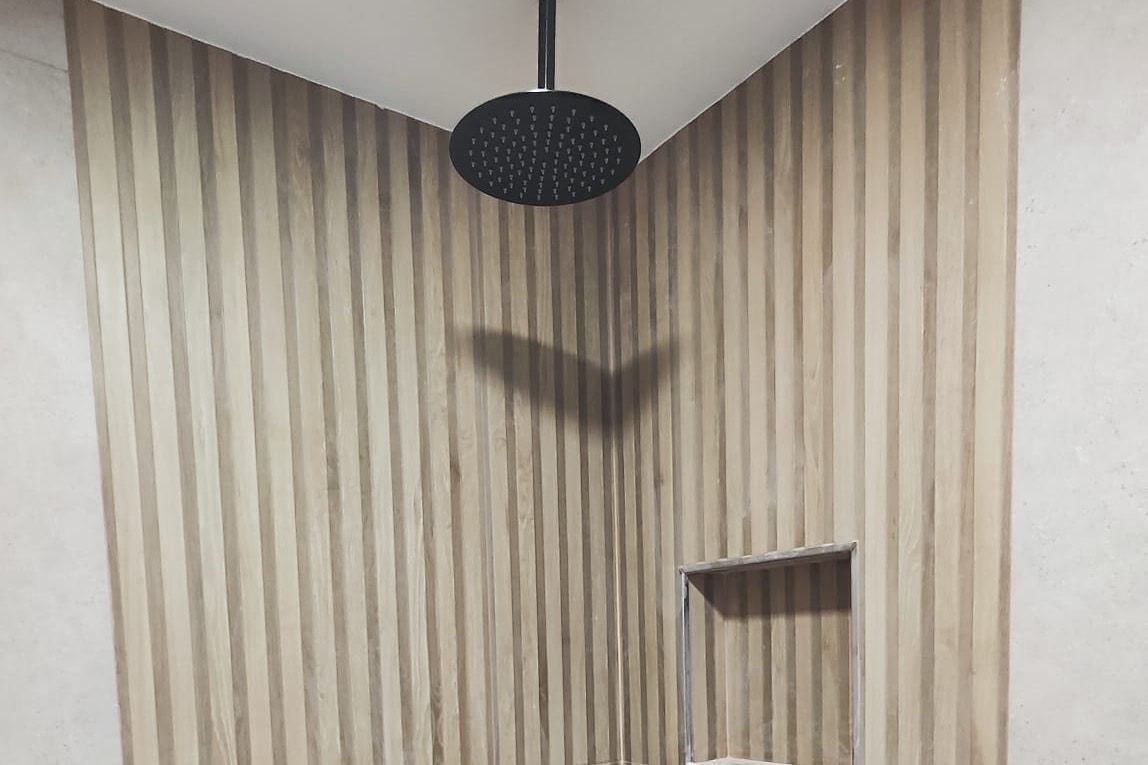 Ducha a ras de suelo con rociador de techo, listones efecto madera y hornacina