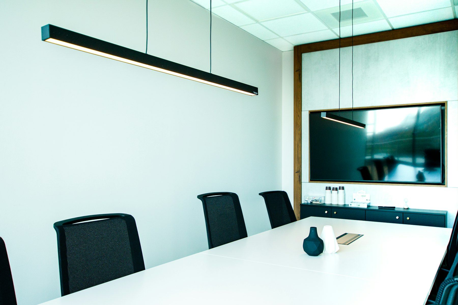 Sala de reuniones blanca con lámpara lineal colgada sobre la mesa