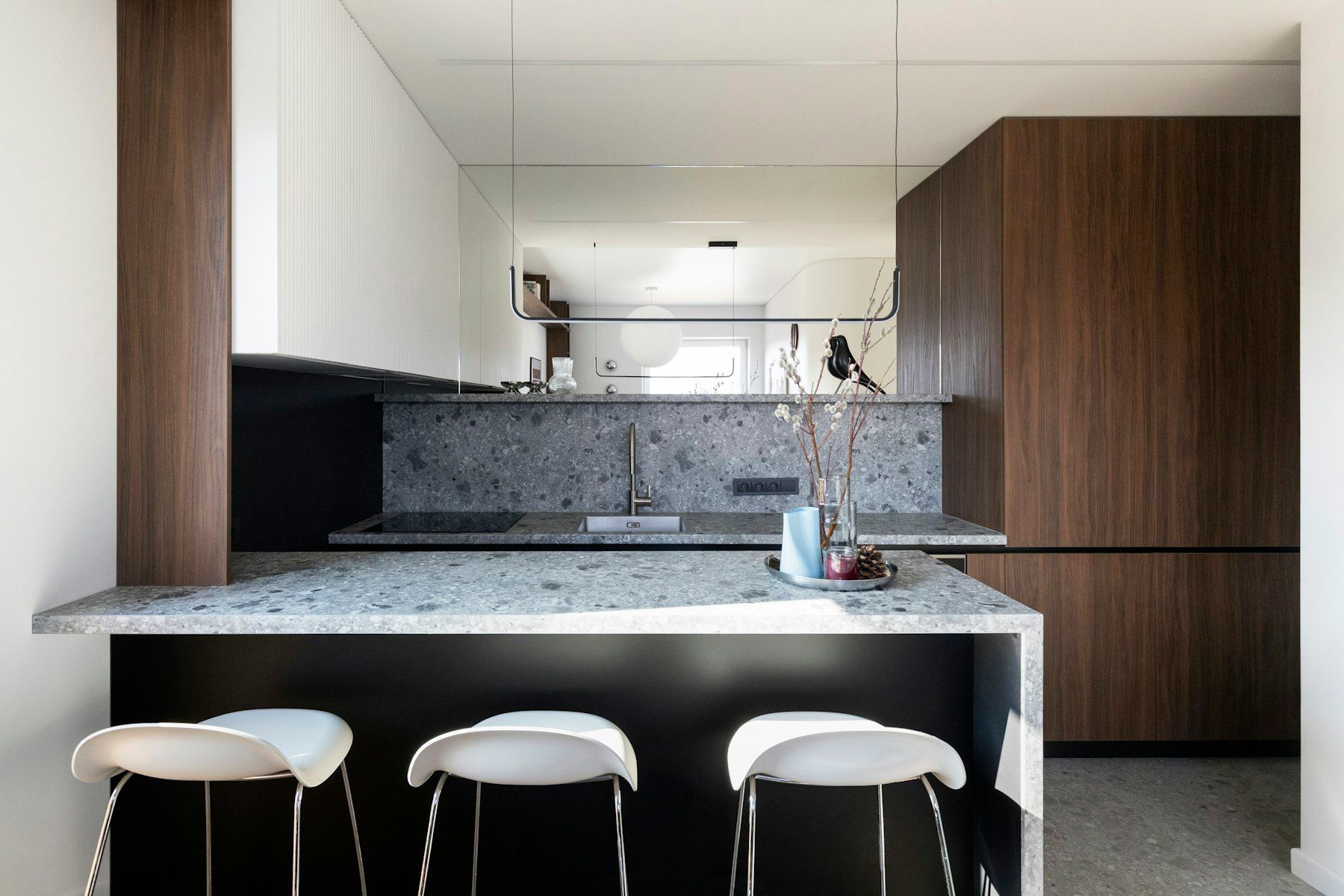 Cocina con península de terrazo, taburetes blancos y muebles de madera