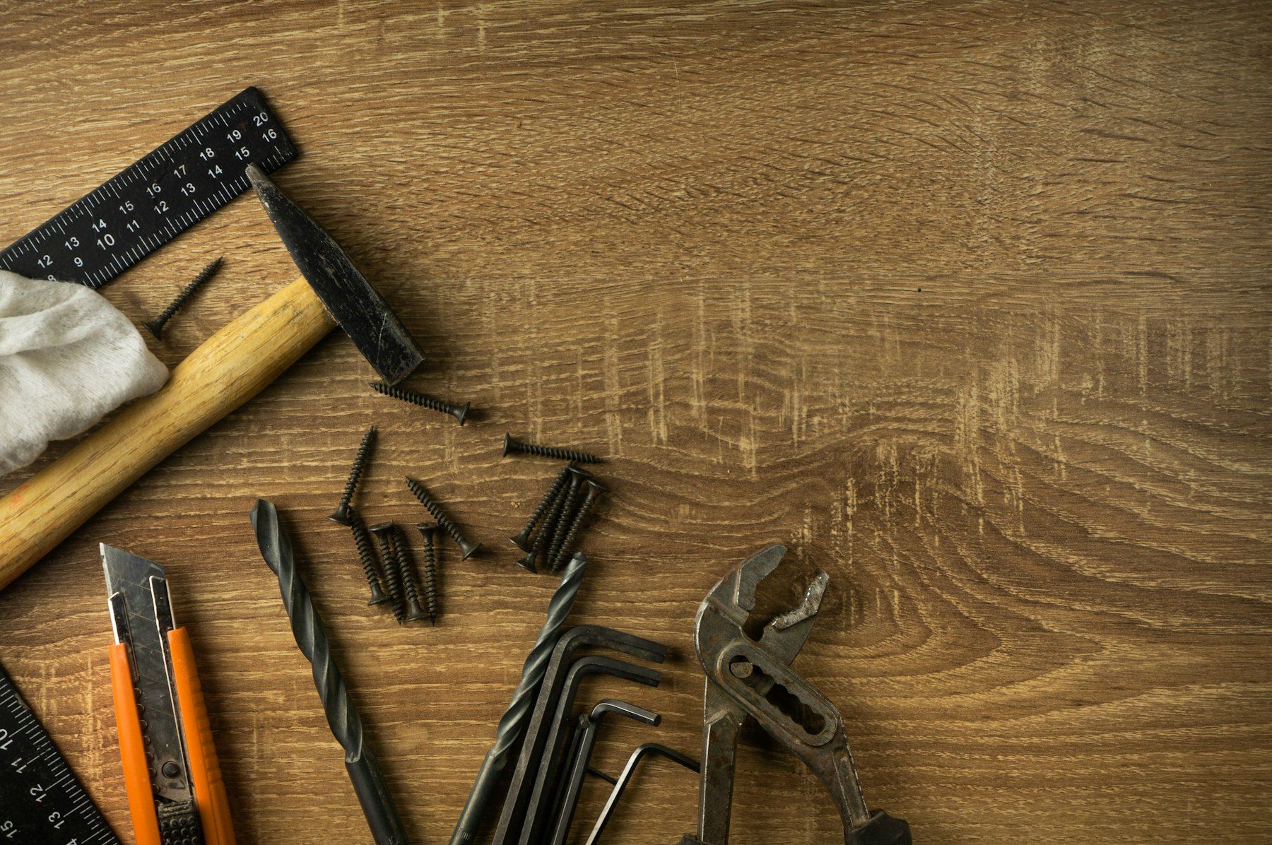 Escuadra, martillo, cúter, brocas y alicates sobre una mesa de madera